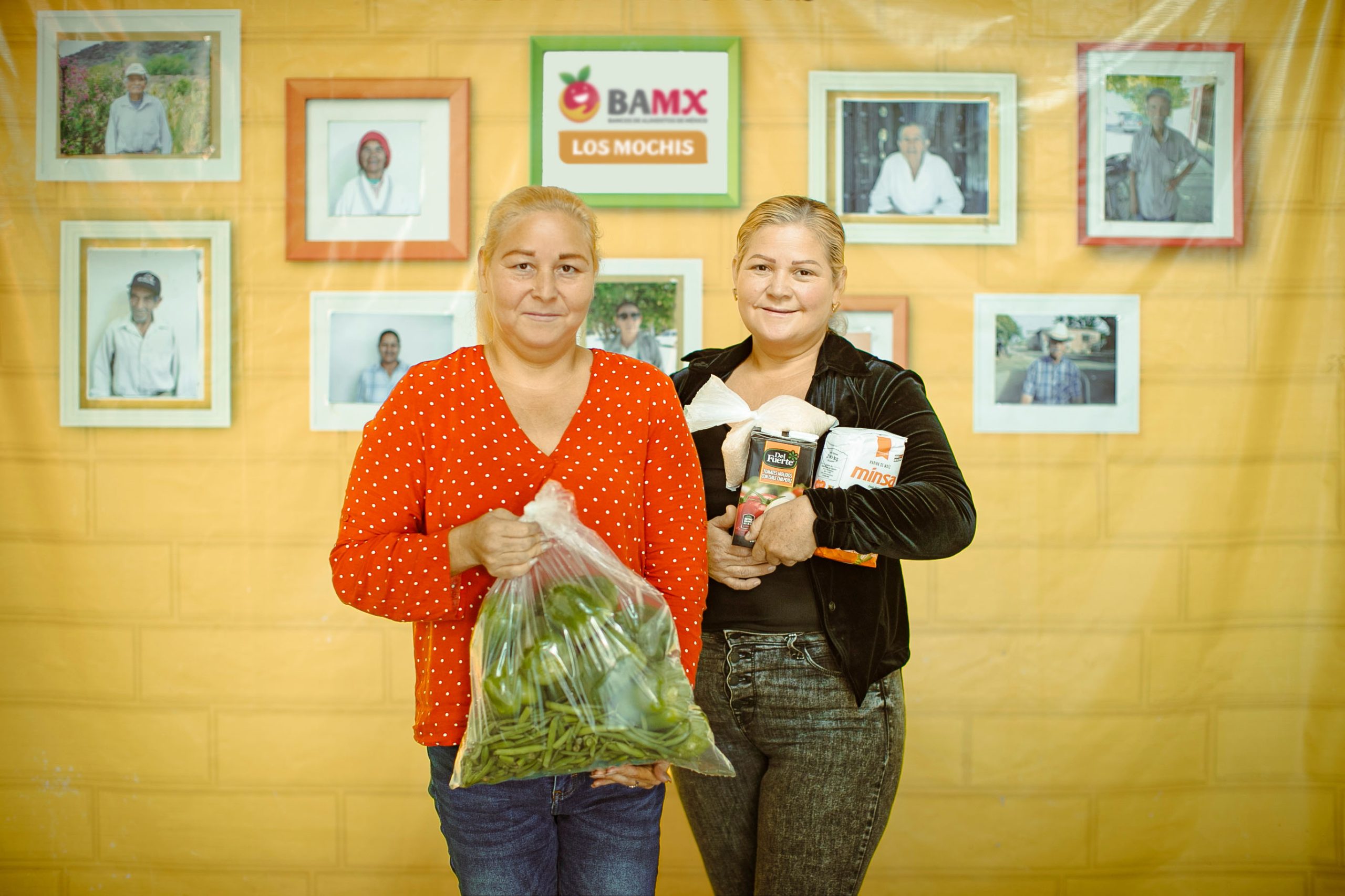 Dos beneficiarias con nuestro paquete alimentario, con fondo de fotografías del programa YO INVITO.